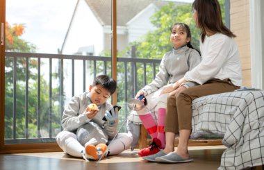 Bir kız ve oğlan, anneleriyle eskrim kıyafetleri içinde yaklaşan müsabakaya hazırlanmak için eskrim antrenmanından önce yiyecek ve spor malzemeleri hazırlıyorlar.