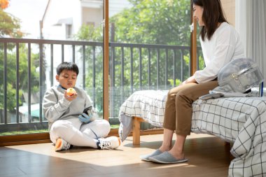 Eskrim kıyafeti giymiş bir çocuk anneleriyle birlikte yaklaşan müsabaka gününe hazırlanmak için eskrim antrenmanından önce yiyecek ve spor malzemeleri hazırlıyor.