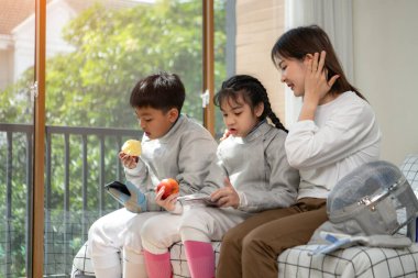 Bir kız ve oğlan, anneleriyle eskrim kıyafetleri içinde yaklaşan müsabakaya hazırlanmak için eskrim antrenmanından önce yiyecek ve spor malzemeleri hazırlıyorlar.