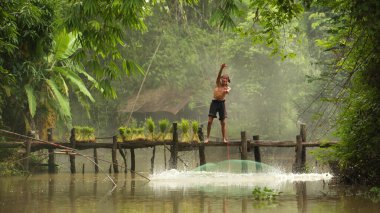 Köprünün tepesinde balıkçı, nehirde balık ağıyla balık tutuyor.