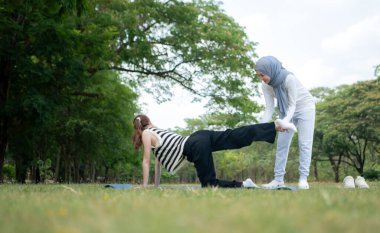 İki genç Müslüman kadın halka açık bir parkta dinleniyor ve egzersiz yapıyor.