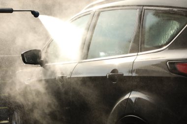 Bir adam arabasını dikkatlice ve sevgiyle yıkamak için basınçlı çamaşır makinesini kullanır. (oto yıkamada dizinin bir bölümü)