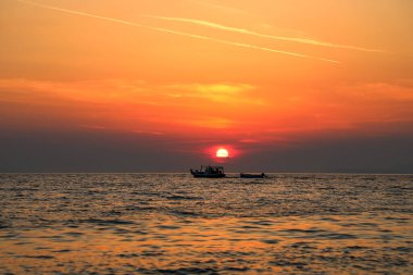 Bir deniz botu Adriyatik Denizi 'nde güzel bir gün batımının arka planında bir tekneyi çekiyor..