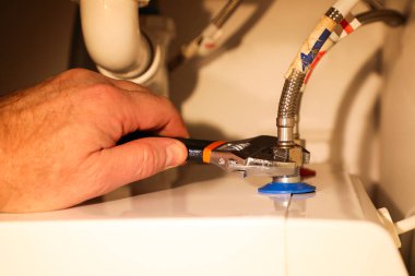 Profesyonel bir muslukçu, ayarlanabilir bir anahtar kullanarak sıcak ve soğuk su hortumlarını kazana bağlar..