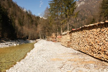 Satılığa hazır odun yığınları bir dağ nehrinin kıyısındaki kereste fabrikasında yatıyor..