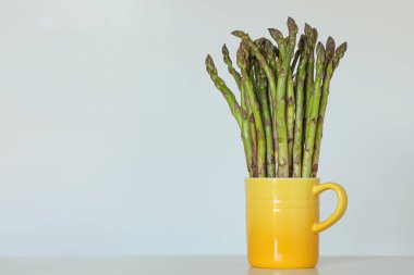 Hafif arka planda sarı bir fincanda duran kuşkonmazlı orijinal natürmort