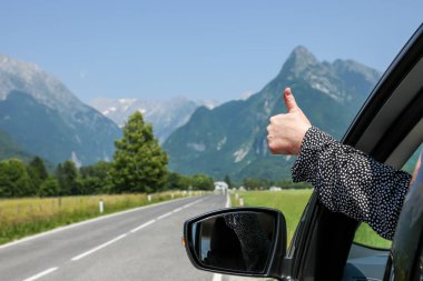 Avrupa Alpleri 'nde güzel bir yol boyunca araba sürerken kadın bir sürücü elini arabanın camından dışarı çıkardı ve her şeyin yolunda olduğunu belirterek baş parmağını kaldırdı..