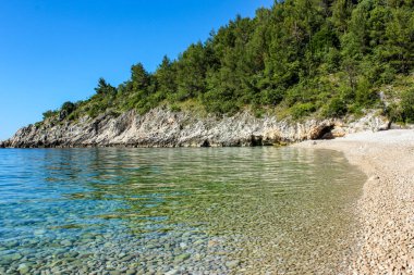 Sakin çakıl taşı plajı ve bereketli ormanlarla çevrili turkuaz deniz ve parlak mavi gökyüzünün altındaki kayalık uçurumlar. Doğayı gözler önüne sermek, sahil seyahati ve huzurlu yaz kaçamakları için mükemmel..