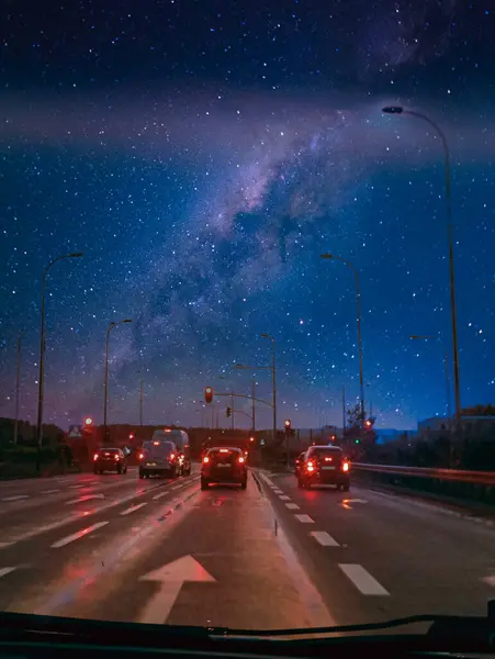 Gece vakti, canlı Samanyolu Galaksisi 'nin altında ıslak yolda giden arabaların sokak lambaları ve trafik ışıklarıyla aydınlatıldığı sahneler. Şehir çevreleri yıldızlı gökyüzünün göksel güzelliğiyle birleşir..