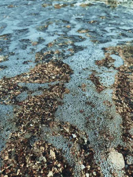 Makro deniz köpüğü ve sığ kıyı sularının altında küçük çakıl taşları. Doğal ışık dokuları ve şeffaflığı arttırır. Denizcilik, tatil, rahatlama ve doğa kavramları için ideal..