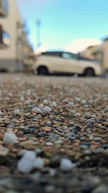 Dolu taşları ve küçük çakıl taşlarıyla kaplı Islak Asfalt 'ın yakın görüntüsü. Bulanık Arkaplan Özellikleri Şehir Elementleri Binalar ve Park Aracı da dahil. Açık havada gündüz vakti yakalandılar.