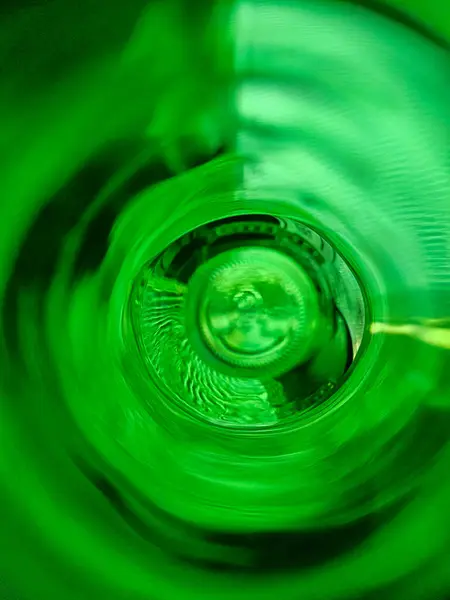Dalgalanan desenler ve ışık yansımaları olan yeşil bir şişeden soyut görüntü. Gün ışığında yakalanan bu resim, benzersiz bir bakış açısı ve canlı bir yeşil renk sunuyor..