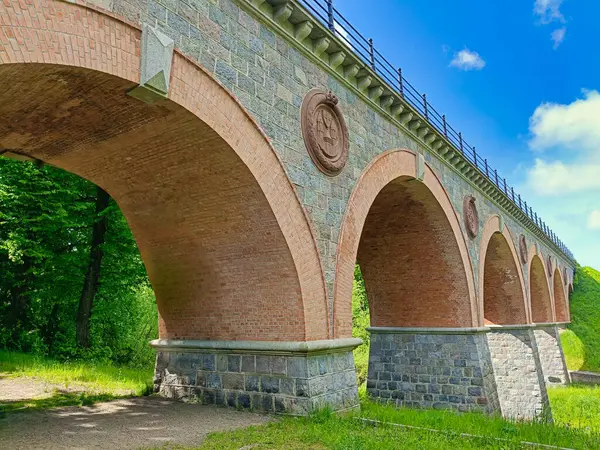 Kırmızı tuğla ve taştan yapılmış tarihi kemerli demiryolu köprüsü güneşli bir günde alçak bir açıdan çekildi. Sütunları süsleyen dekoratif madalyonlar. Mimarlık, mühendislik, miras ve seyahat konularına uygundur..