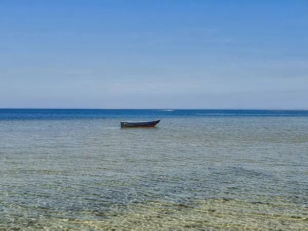 Sakin sığ denizde, berrak mavi gökyüzünün altında kristal berrak suyla yüzen ıssız ahşap bir tekne. Gün ışığında yakalanan huzurlu deniz manzarası. Kavram: yalnızlık, doğa, minimalizm, seyahat.