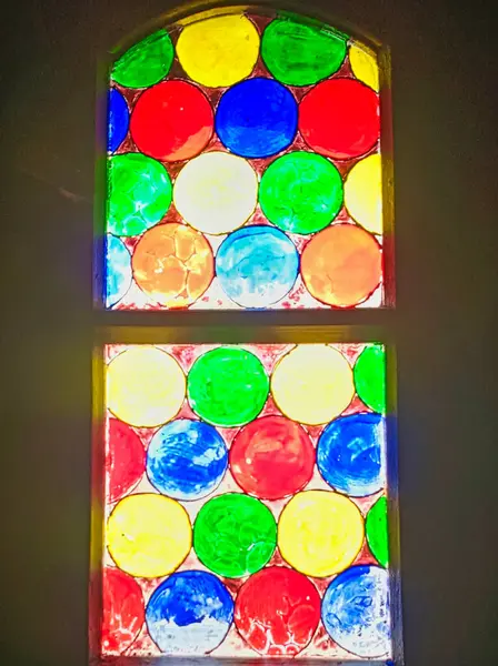 Kırmızı, mavi, yeşil ve sarı dairesel desenli renkli vitray. Camdan geçen güneş ışığı. Kapalı alanda çekilmiş. Sanat, gelenek, tasarım ve maneviyat temaları için ideal.