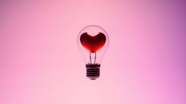 Cam ampulün içinde kalp şeklinde lifli ampul metal tabanlı ve pembe arkaplandaki destek kabloları ampul hatlarını ve taban vidalarını gösteriyor.