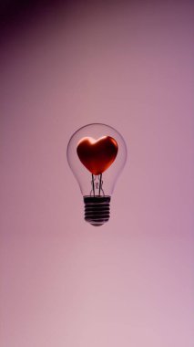 Cam ampulün içinde kalp şeklinde lifli ampul metal tabanlı ve pembe arkaplandaki destek kabloları ampul hatlarını ve taban vidalarını gösteriyor.