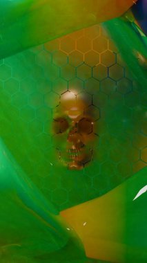 İnsan kafatası formu, yarı saydam yeşil sıvı şekillerle çevrili altıgen desen ızgarasının arkasında belirir.