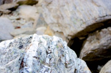 Beyaz kuvars damarları ve doğal mineral desenleri olan engebeli kaya yüzeyine yakın çekim, jeolojik detay ve toprak dokusunu gösteriyor..