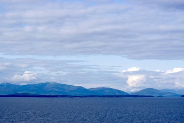 Alaska 'nın dinamik bulutlar altında dönen dağ sıralarının yer aldığı sakin kıyı şeridinin çarpıcı bir görüntüsü. Bir yolcu gemisinden Skagway yakınlarında yakalanan bu görüntü Alaska 'nın doğal güzelliğinin ve uçsuz bucaksız vahşi doğasının altını çiziyor.