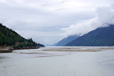 Alaska 'nın Skagway yakınlarındaki sakin kıyı şeridinin büyüleyici siyah beyaz bir görüntüsü, sisli dağları, sakin su yollarını ve dramatik zıtlıkları barındırıyor. Bu minimalist kompozisyon, Alaska çölünün el değmemiş güzelliğini vurguluyor.