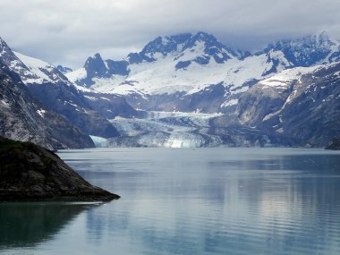 Dramatik bir buzulun yansıması Buzul Körfezi 'nin durgun suları, karla kaplı tepelerle çevrili kasvetli bir gökyüzünün altında..