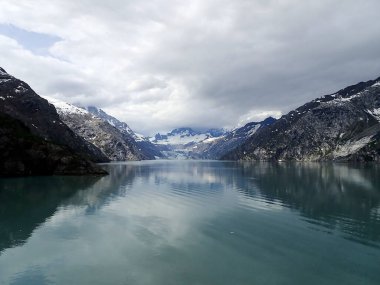 Alaska, Glacier Körfezi 'ndeki yüksek tepeler arasında uzanan bir buzulun yansıması aşağıdaki sakin sularda parıldıyor..