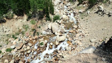 Etrafı toprakla çevrili ve yemyeşil yemyeşil yeşermiş dağılmış kayaların üzerinde dalgalı bir dere. Engebeli dağ güzelliğinin mükemmel tasviri..