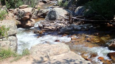 Dalgalı aksanlı kayaların üzerinden akan, engebeli arazilerle çevrili, güneşli bir dağ deresi. Temiz su, doğanın dingin güzelliğinde çağlarken ışıldıyor..