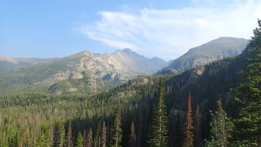 Berrak mavi gökyüzünün altında gür çam ormanlarıyla çevrili çarpıcı dağ zirveleri, doğanın dinginliğini ve ihtişamını yakalıyor..