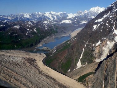 Alaska 'daki Denali Ulusal Parkı' nın yüksek tepelerinin arasına yerleştirilmiş buzul gölü sergilenen çarpıcı bir hava görüntüsü. Manzaralı bir uçuş sırasında yakalanan bu resim, yemyeşil vadiler, kayalık arazi ve buzul kalıntıları arasındaki zıtlığı vurgular. 