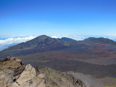 Haleakal Krateri 'nin nefes kesen bu görüntüsü krater tabanından yükselen volkanik kül konilerinin engebeli siyah lav arazisine karşı kırmızımsı renklerini ortaya çıkarıyor. Mauis dağlarının uzak yamaçları
