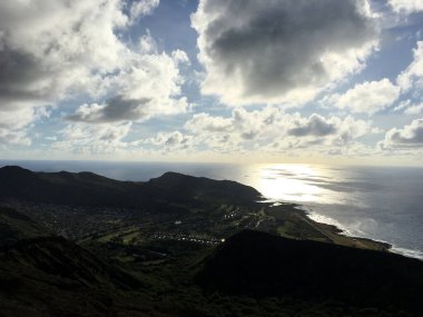 Uçsuz bucaksız mavi gökyüzünün altında dramatik bulutlarla Kilauea Krateri 'nin çarpıcı manzarası. Bu engebeli volkanik arazi yemyeşil bitki örtüsüyle çelişiyor..
