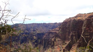 Uçsuz bucaksız mavi gökyüzünün altında dramatik bulutlarla Kilauea Krateri 'nin çarpıcı manzarası. Bu engebeli volkanik arazi yemyeşil bitki örtüsüyle çelişiyor..