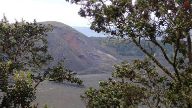 Uçsuz bucaksız mavi gökyüzünün altında dramatik bulutlarla Kilauea Krateri 'nin çarpıcı manzarası. Bu engebeli volkanik arazi yemyeşil bitki örtüsüyle çelişiyor..