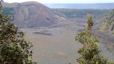 Uçsuz bucaksız mavi gökyüzünün altında dramatik bulutlarla Kilauea Krateri 'nin çarpıcı manzarası. Bu engebeli volkanik arazi yemyeşil bitki örtüsüyle çelişiyor..