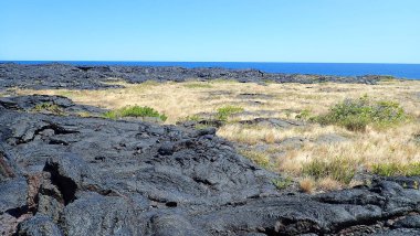 Uçsuz bucaksız mavi gökyüzünün altında dramatik bulutlarla Kilauea Krateri 'nin çarpıcı manzarası. Bu engebeli volkanik arazi yemyeşil bitki örtüsüyle çelişiyor..