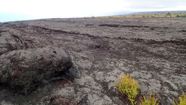 Uçsuz bucaksız mavi gökyüzünün altında dramatik bulutlarla Kilauea Krateri 'nin çarpıcı manzarası. Bu engebeli volkanik arazi yemyeşil bitki örtüsüyle çelişiyor..