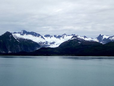 Karanlık ormanlık yamaçlar ve bulutlu gökyüzünün altında karla kaplı engebeli dağlar. Karamsar ışıklandırma, bu buzul arazisinin düşünceli atmosferini arttırıyor. Aşağıdaki buzlu sulara ince bir şekilde yansıyor..