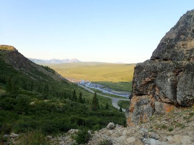 Akşam ışığı Denali Ulusal Parkı 'nda kayalık kayalıklar ve uzak dağ tepeleriyle çevrili yeşil bir Alaska Vadisi' nin içinden geçen dolambaçlı bir nehir..