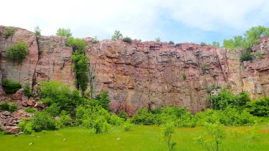Minnesota 'daki Blue Mound State Park' taki çimenli bir çayır ve yoğun bir çalılığın üzerinde yükselen dikey bir kuvart duvarı..