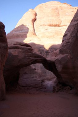 Utah, Arches Ulusal Parkı 'ndaki kumtaşı kanyonunda güneş ışığı ve derin gölgeyle parlayan doğal bir taş kemer.