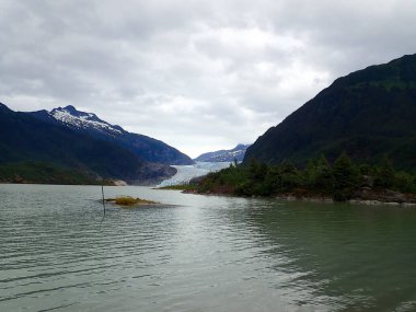 Mendenhall Buzulu 'nun Juneau Alaska' da dramatik bulutlu bir gökyüzünün altında buzul gölüne uzanması geniş bir bakış açısı.