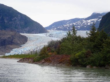 Mendenhall Buzulu 'nun mavi buz yüzünün detaylı görüntüsü Juneau Alaska' daki kayalık kıyı şeridi ve sonsuz yeşil ormanın yanındaki bir göle iniyor.