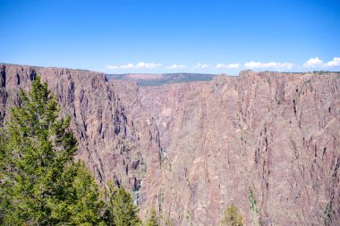 Gunnison Nehri 'nin yukarısındaki devasa uçurum duvarları Kara Kanyon' un derinliklerinde berrak mavi Colorado gökyüzünün altında.