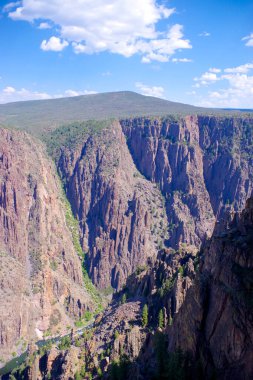 Dikey dik kayalıklar Gunnison 'un Kara Kanyonu' nun derinliklerindeki sarmal Gunnison Nehri 'ni parçalı bulutlu bir gökyüzünün altında çerçeveletir.