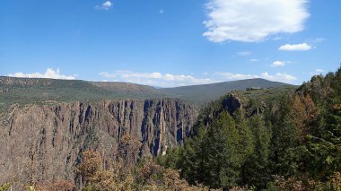 Kara Kanyon 'un dramatik uçurumları ve mavi gökyüzünün altındaki yeşil ormanlarla panoramik görüntüsü.