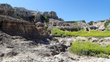 Uçurumlar ve katmanlı kaya oluşumları Çorak Topraklar Ulusal Parkı 'ndaki açık mavi gökyüzünün altında sarı çayır çiçeklerinin üzerinde yükseliyor.