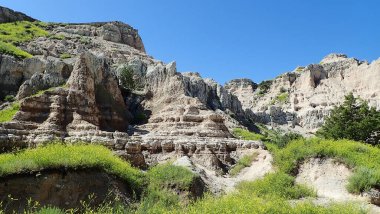 Erimiş kaya izmaritleri ve katmanlı uçurumlar Badlands Ulusal Parkı 'ndaki canlı yeşil ve sarı çayır bitkilerinin ceplerini sarıyor.