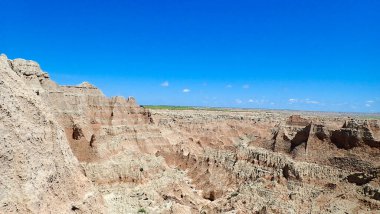 Engebeli çorak arazi manzarası katmanlı kaya oluşumları ve parlak mavi gökyüzünün altında aşınmış derin vadiler.